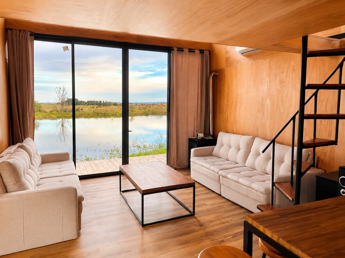 Living terminado de cabaña con grandes ventanales y vista al lago